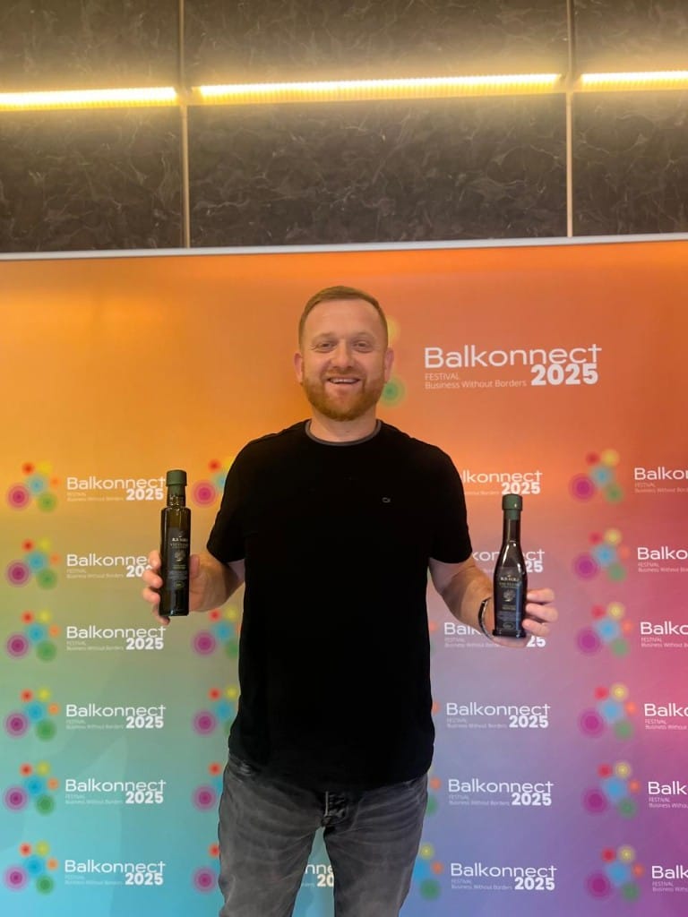Smiling ambassador with two dark glass bottles of olive oil beside the Balkonnect step and repeat